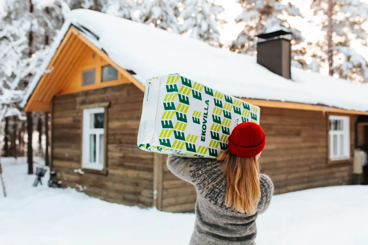 Person bär EKOVILLA-säck till ett snötäckt hus